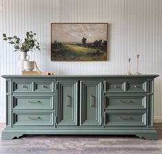 an old dresser painted green with gold handles and drawers on the bottom, in front of a painting