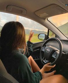 a woman sitting in the driver's seat of a car with her hand on the steering wheel