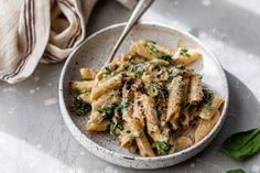 a white bowl filled with pasta and spinach on top of a table next to a napkin