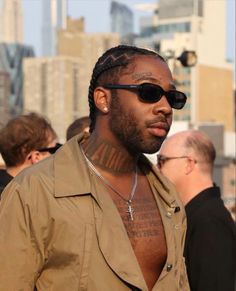 a man with tattoos on his chest standing in front of other men and wearing sunglasses