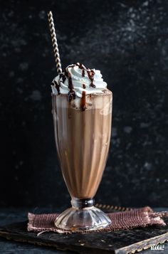 a tall glass filled with chocolate milkshake and whipped cream, on top of a table