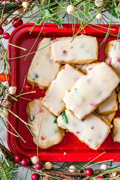 christmas cookies with white icing and sprinkles in a red tray surrounded by greenery