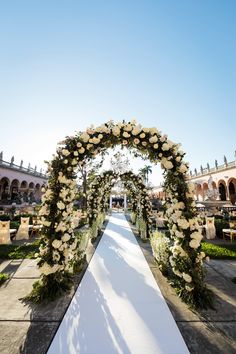 an outdoor ceremony setup with white flowers and greenery on the aisle, in front of a building