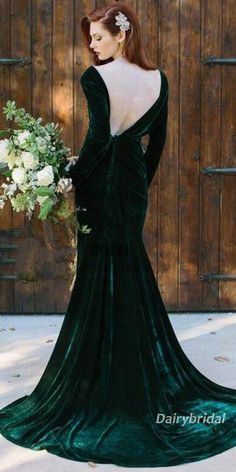 a woman in a long green dress standing next to a wooden door and holding a bouquet