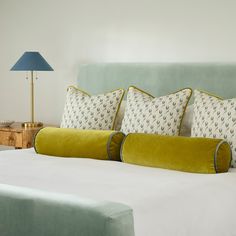 a bed with two pillows on top of it next to a night stand and lamp