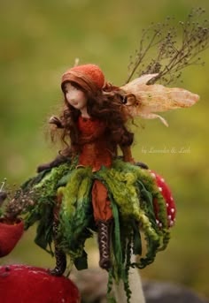 the doll is wearing a red hat and green dress with feathers on it's wings