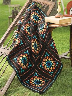 a crocheted blanket sitting on top of a wooden bench next to a book