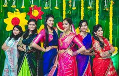 women in colorful sari standing next to each other with flowers on the wall behind them