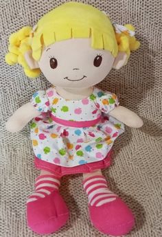 a stuffed toy doll with yellow hair and pink shoes on a white surface next to a gray blanket