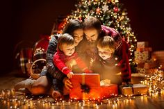 a family opening a christmas present in front of a christmas tree with lights on it