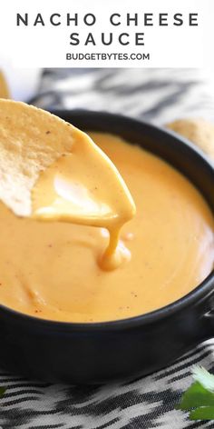 a tortilla chip being dipped with nacho cheese sauce in a black bowl