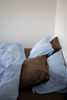 an unmade bed with blue sheets and brown pillows