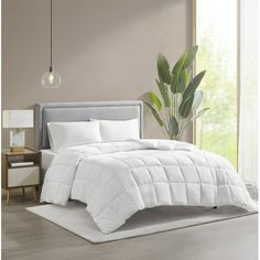 a white comforter on a bed in a room with wood floors and plants next to it