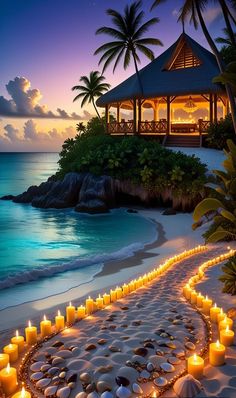 many candles are lit on the sand near the water and beach at night, with a gazebo in the background