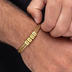 a man wearing a gold bracelet with words written on it and an arrow in the middle