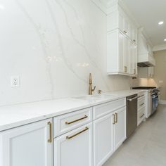 a kitchen with white cabinets and marble counter tops, gold pulls on the faucets