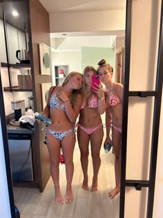 three women in bikinis taking a selfie in the bathroom mirror with their cell phone