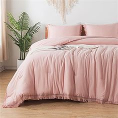 a bed with pink comforter and pillows in a room next to a potted plant