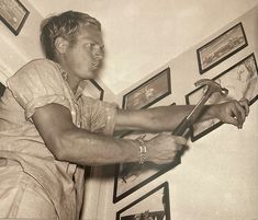 an old photo of a man holding a pair of scissors in his right hand while leaning against the wall