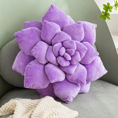 a purple flower pillow sitting on top of a gray couch next to a white glove