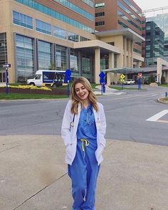 a woman standing on the sidewalk in front of a building wearing scrubs and blue overalls