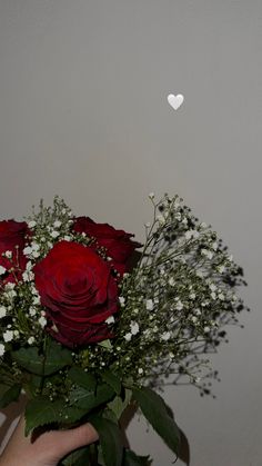 a bouquet of roses and baby's breath in someones hand with a heart on the wall