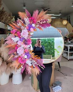 a woman taking a selfie in front of a mirror with pink and purple flowers