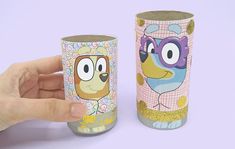 a hand is holding two toilet paper rolls with cartoon characters on them, one has an owl and the other has a dog