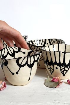 a hand is picking up some black and white bowls with flowers on the table next to them