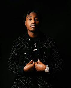 a man with his hands folded in front of him, standing against a black background