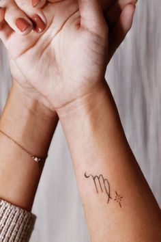 two women holding hands with tattoos on their wrists and one has a zodiac sign tattooed on the wrist