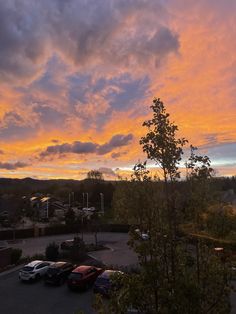 a parking lot filled with lots of parked cars under a cloudy blue and orange sky