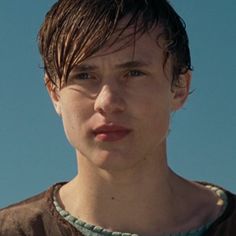 a close up of a person wearing a brown shirt and green necklace with blue sky in the background