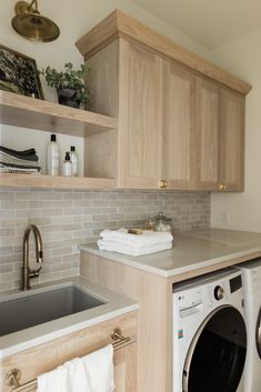 a washer and dryer in a small room with wooden cabinets, white counter tops and gray tile backsplash