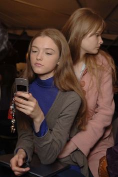 two women sitting next to each other looking at a cell phone