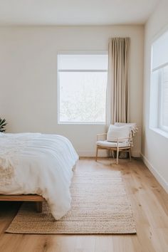 a bedroom with a bed, chair and rug on the hardwood floor in front of a window