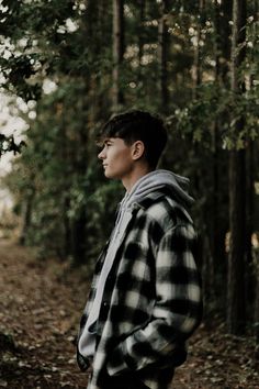 a young man standing in the middle of a forest looking off into the distance with trees and leaves all around him