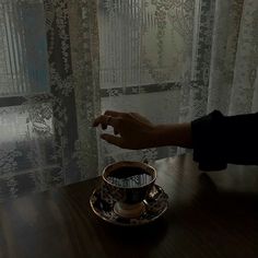 a person reaching for something in a coffee cup on a table next to a window