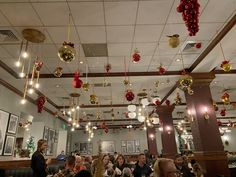 people sitting at tables in a restaurant with christmas decorations hanging from the ceiling above them