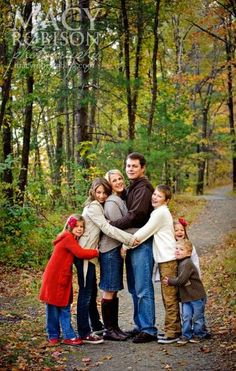 a family posing for a photo on a path in the woods with fall leaves around them