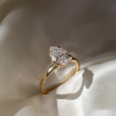 a gold ring with a pear shaped diamond on it's side sitting on a white cloth