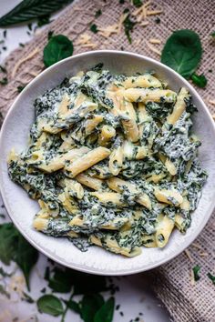 a white bowl filled with pasta and spinach on top of a cloth covered table