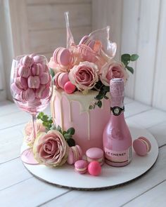 a pink cake with roses and macaroons on it, next to a bottle of champagne