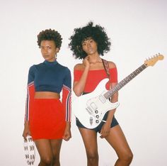 two young women standing next to each other with guitars in their hands and one holding an electric guitar