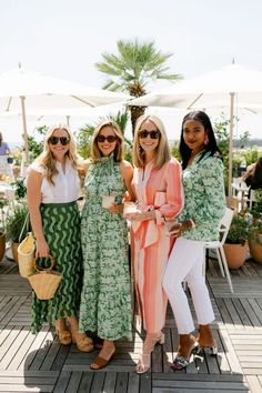 three women standing next to each other in front of an open air area with palm trees