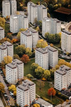 an aerial view of some very tall buildings in the fall season with trees and cars parked on the street