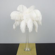 a tall vase with white feathers in it on a yellow place mat next to a gray wall