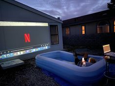 a man sitting in an inflatable pool with a laptop on his lap while watching tv