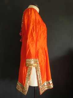 "The embellishment on this stunning outfit is magnificent! It's a very dramatic show-stopper outfit for a special occasion, when you want to make a statement. The mirror-work is made using real mirror glass! Kameez/Top is made of orange silk. The sleeves are not lined and so are somewhat sheer. There is minor staining under the arms. Features: ♦ wire embroidered mirror-work ♦ copper silk pleated ribbon trim ♦ sweetheart neckline trimmed w/ gold metal disc beads and magenta silk piping ♦ high sid Festive Raw Silk Sharara With Cutdana Details, Orange Kurta With Gota Work In Traditional Drape, Bollywood Style Designer Anarkali Set, Bollywood Style Anarkali Set For Designer Festivals, Designer Bollywood Sharara For Navratri, Bollywood Style Designer Sharara For Navratri, Tissue Silk Straight Kurta With Mirror Work, Festive Raw Silk Sharara With Gota Work, Designer Bollywood Anarkali Set For Festivals