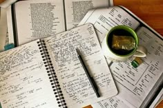 an open notebook sitting on top of a wooden table next to a cup of coffee